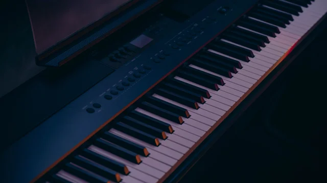 Piano keys lit by soft blue and pink light in a dark room.