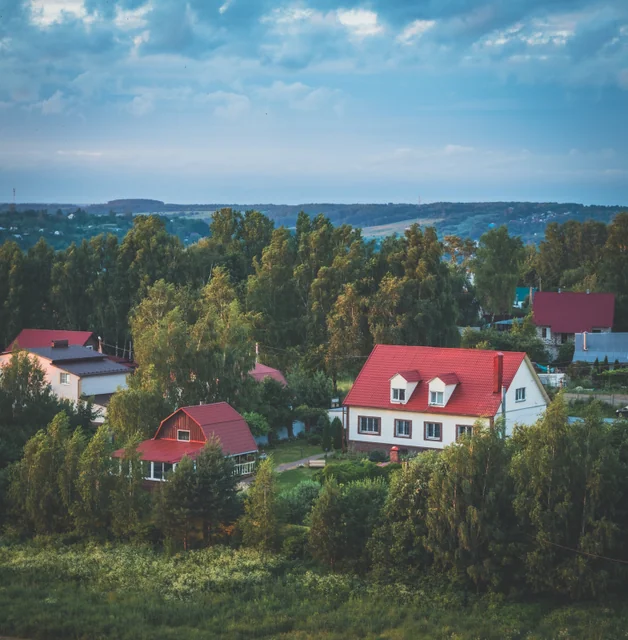 Houses with red roofs sit among trees beneath distant green hills.