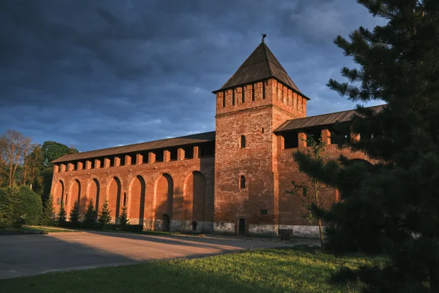 Warm sunlight falls on a red-brick fortress wall and tower beneath dark clouds.