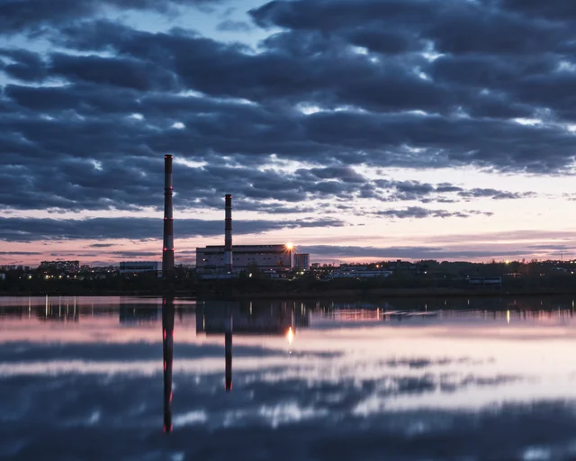 Industrial chimneys and evening clouds reflected in still water.