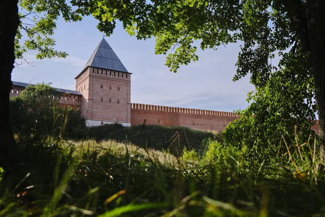 A brick tower and fortress wall surrounded by summer greenery.