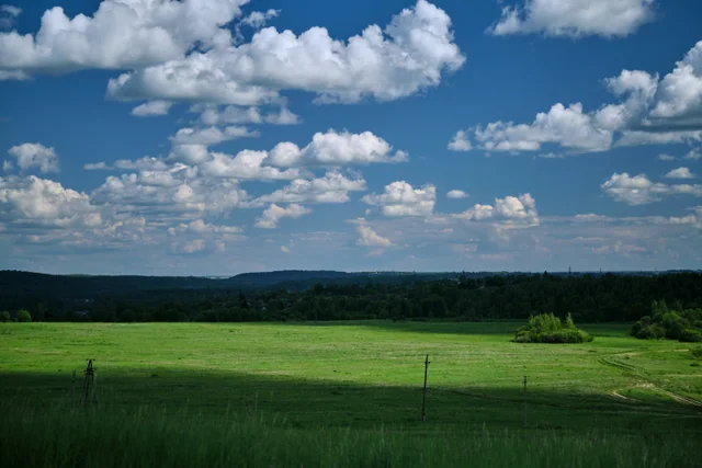 Sunlit green fields beneath a wide blue sky filled with clouds.