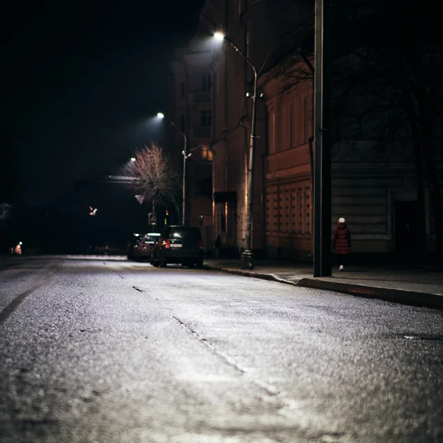 A quiet wet street lit by lamps beside an old brick building at night.