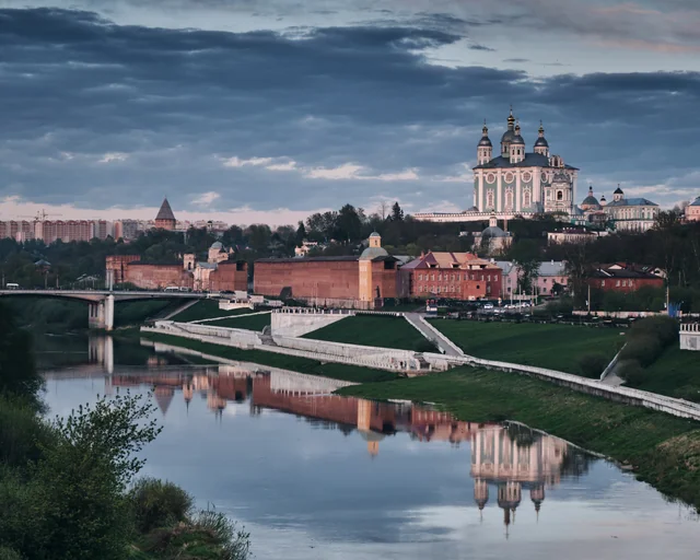 A cathedral and old city walls reflected in a quiet river at dusk.