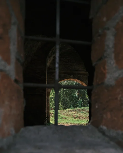 A small arched opening reveals trees beyond a dark brick wall.